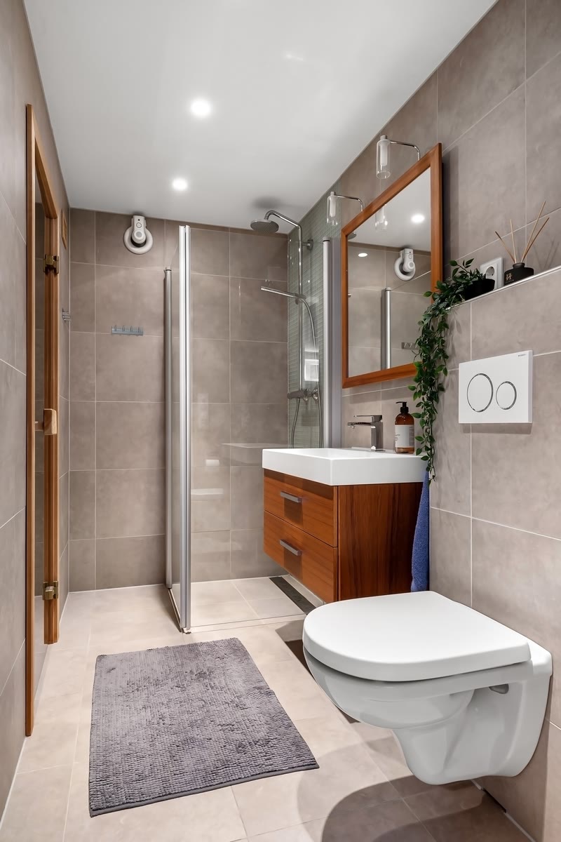 A tiled bathroom with a glass shower enclosure, vanity and toilet.
