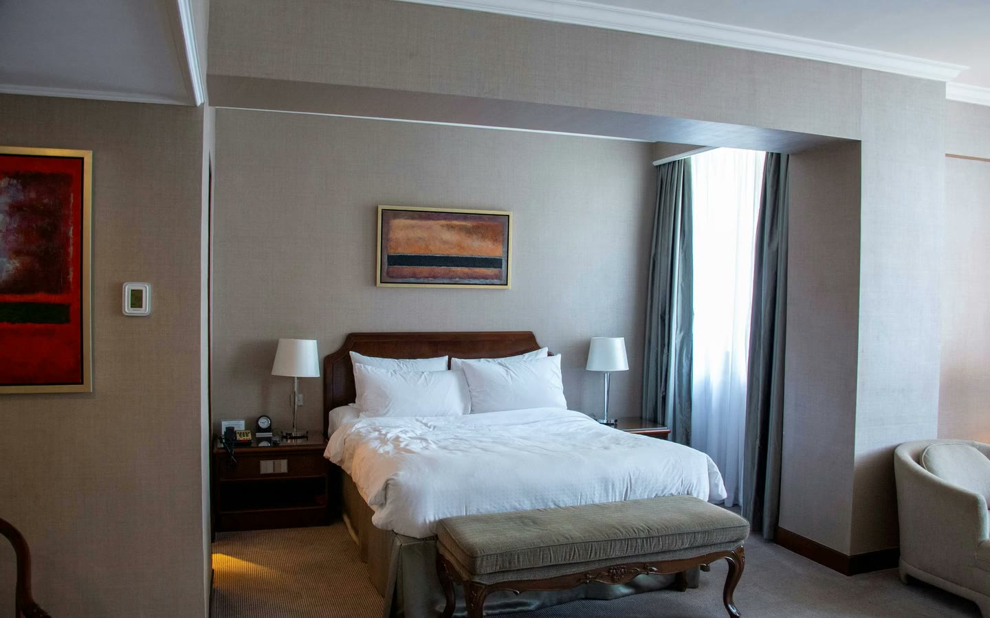 First frame of the sequence: a white bed with a bench, bedside lamps and a large window.