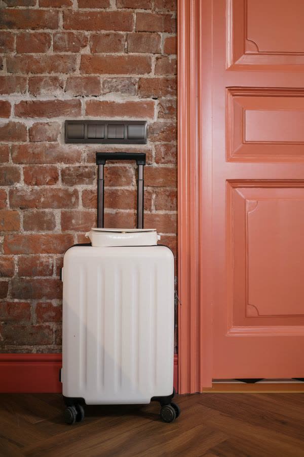 White suitcase by a brick wall and a coral door