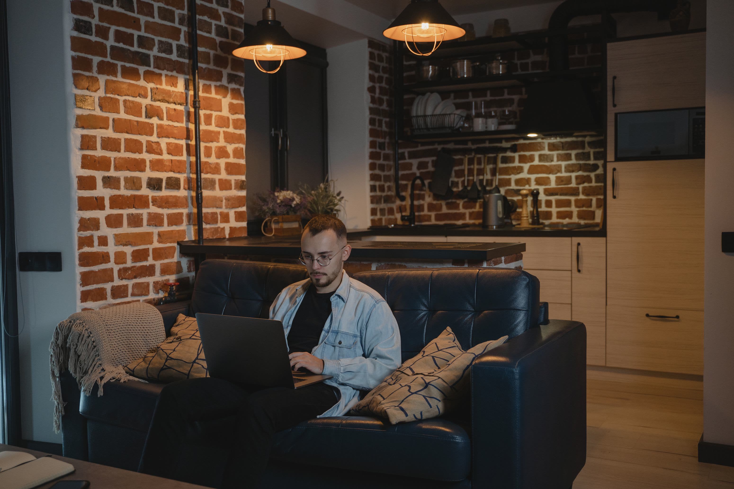 A guest working on a laptop on the sofa of a brick-walled suite