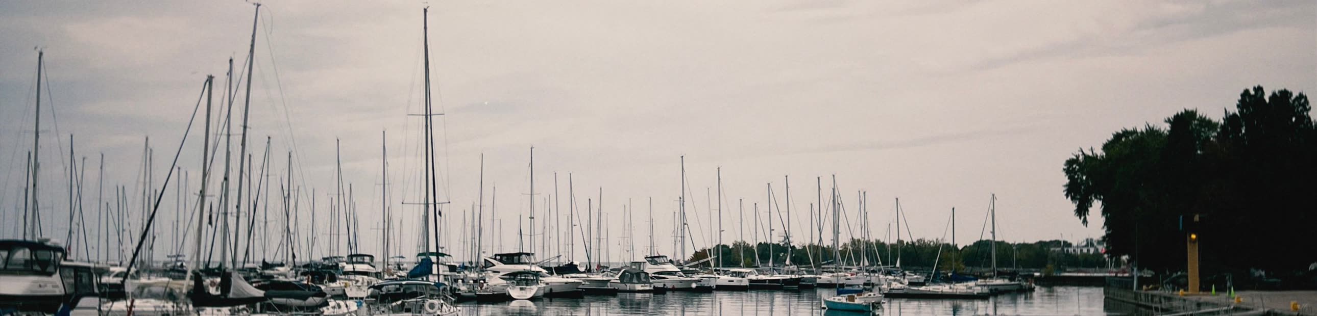 Sailboats moored in a calm harbor under a grey sky