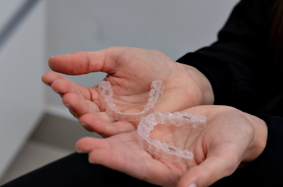 A pair of clear aligner trays in open hands