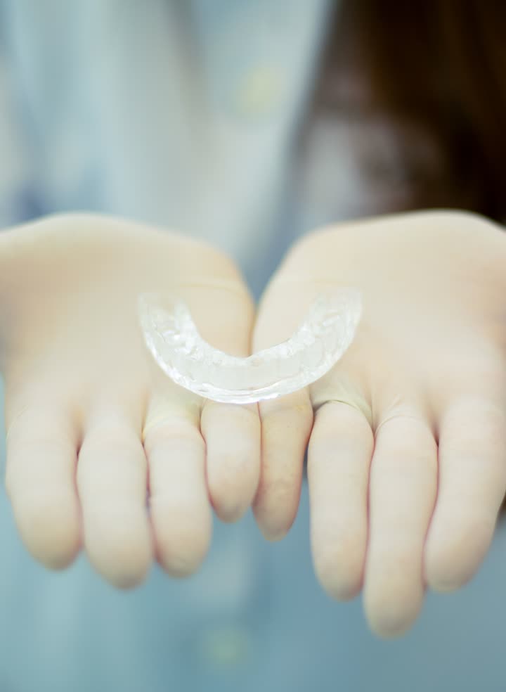A clear aligner tray in gloved hands
