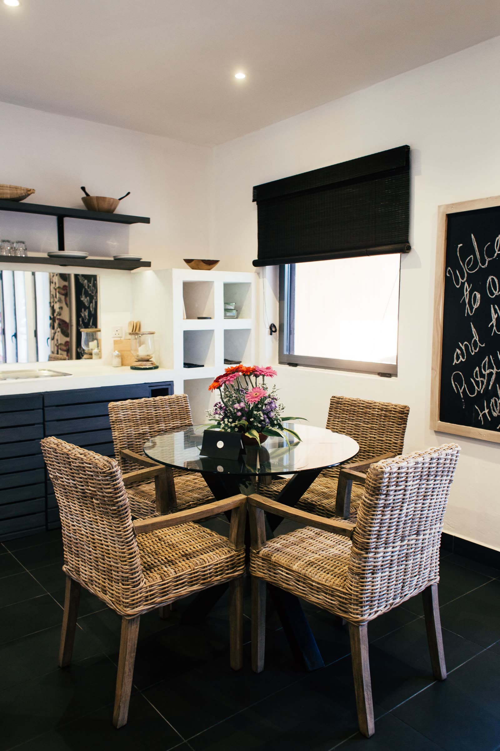 The white dining room with its open kitchen window, marble counter and a tall vase of flowers