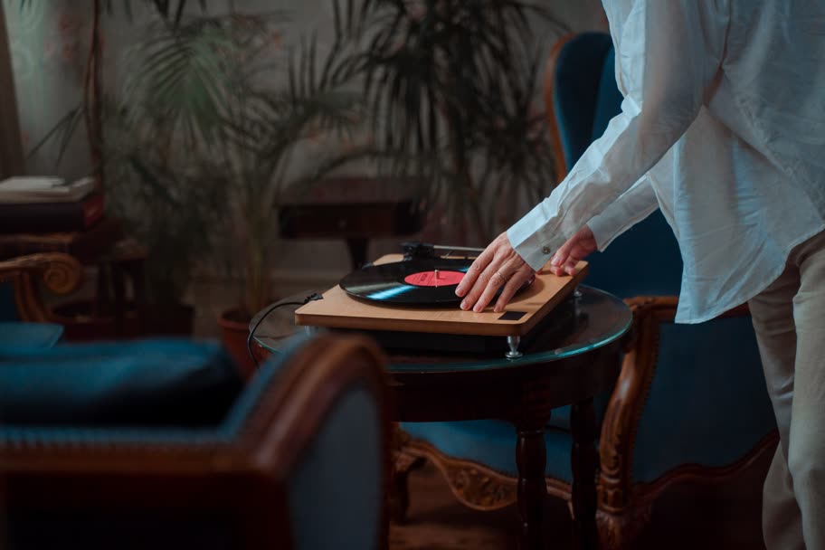 A hand lowering the tonearm on a wooden turntable in a dim room