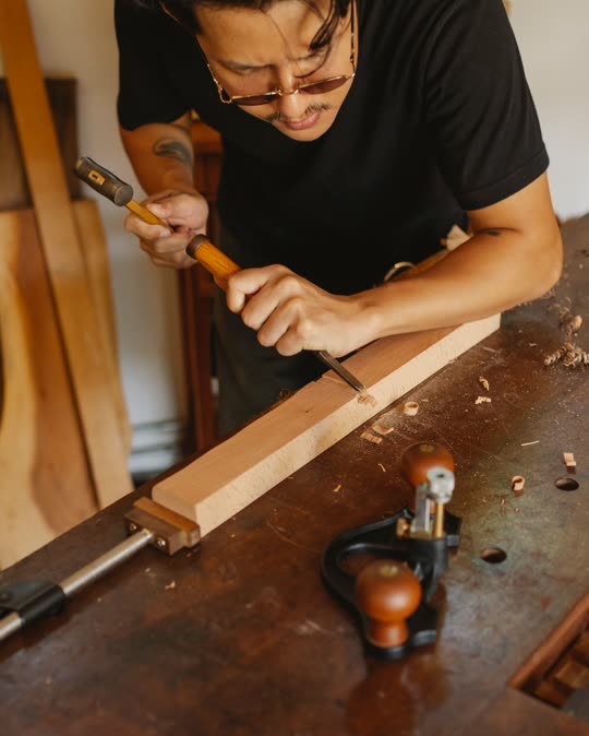 A woodworker chiselling a board at a bench