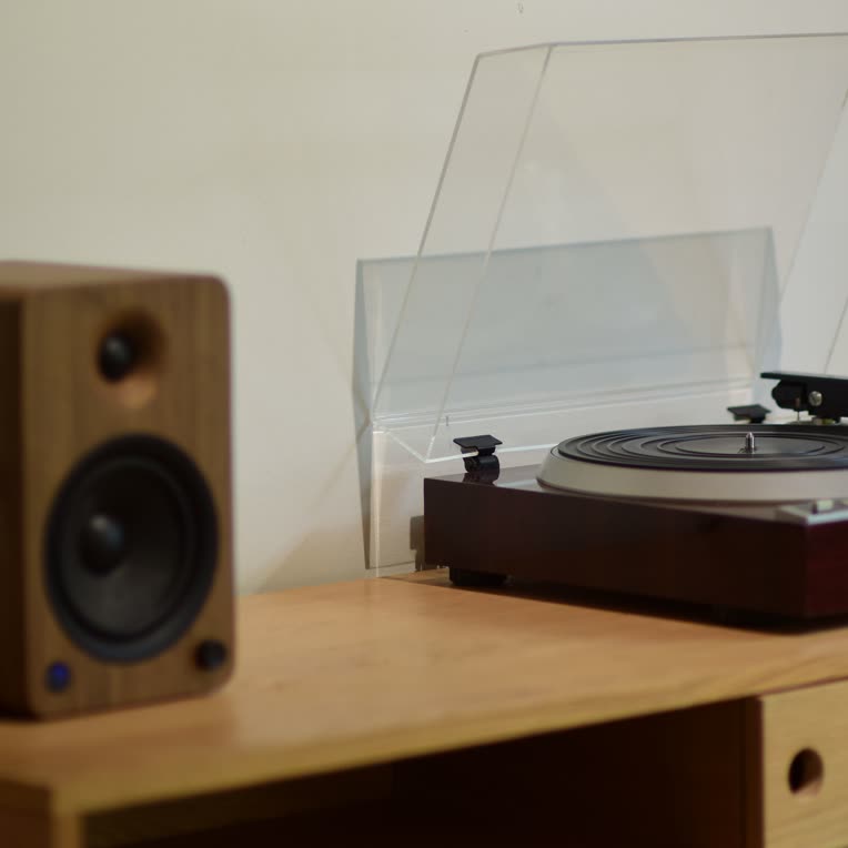 A wooden speaker and a turntable on a light oak sideboard