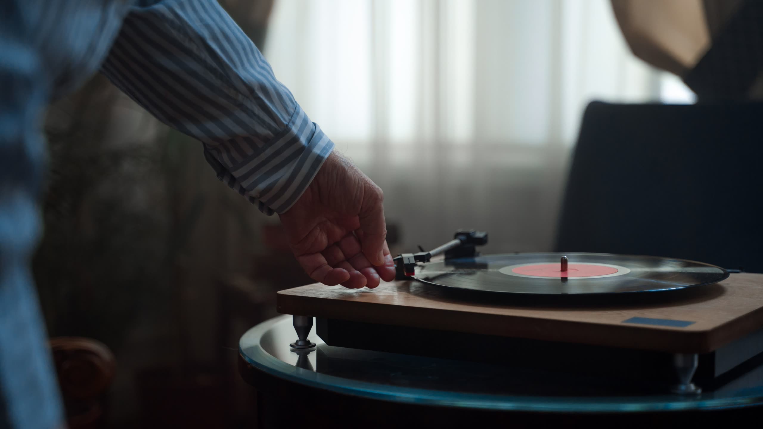 A hand setting the needle on a turntable by a window