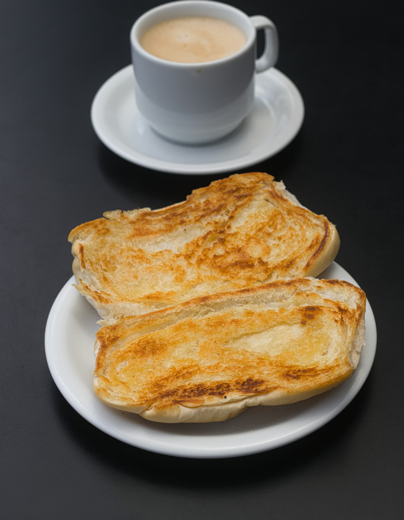 Pressed buttered bread on a white plate with a cup of café con leche