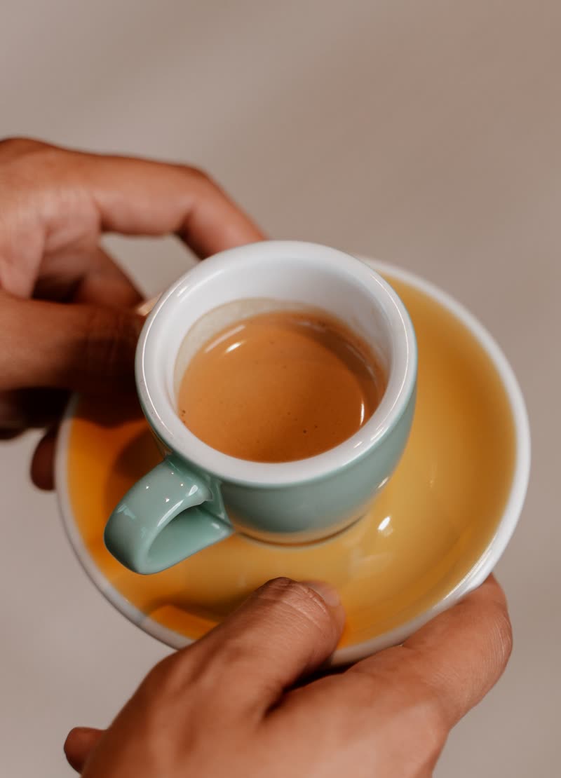 Two hands holding a small cup of coffee on a yellow saucer
