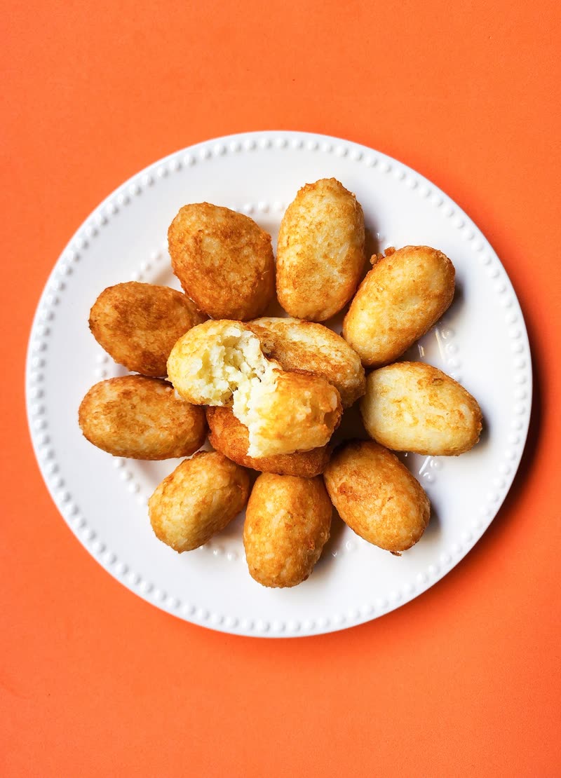 A plate of golden croquetas, one broken open, on an orange table