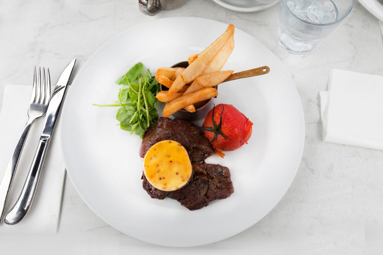 A sliced steak with béarnaise on a plate at a set table, glasses beside it
