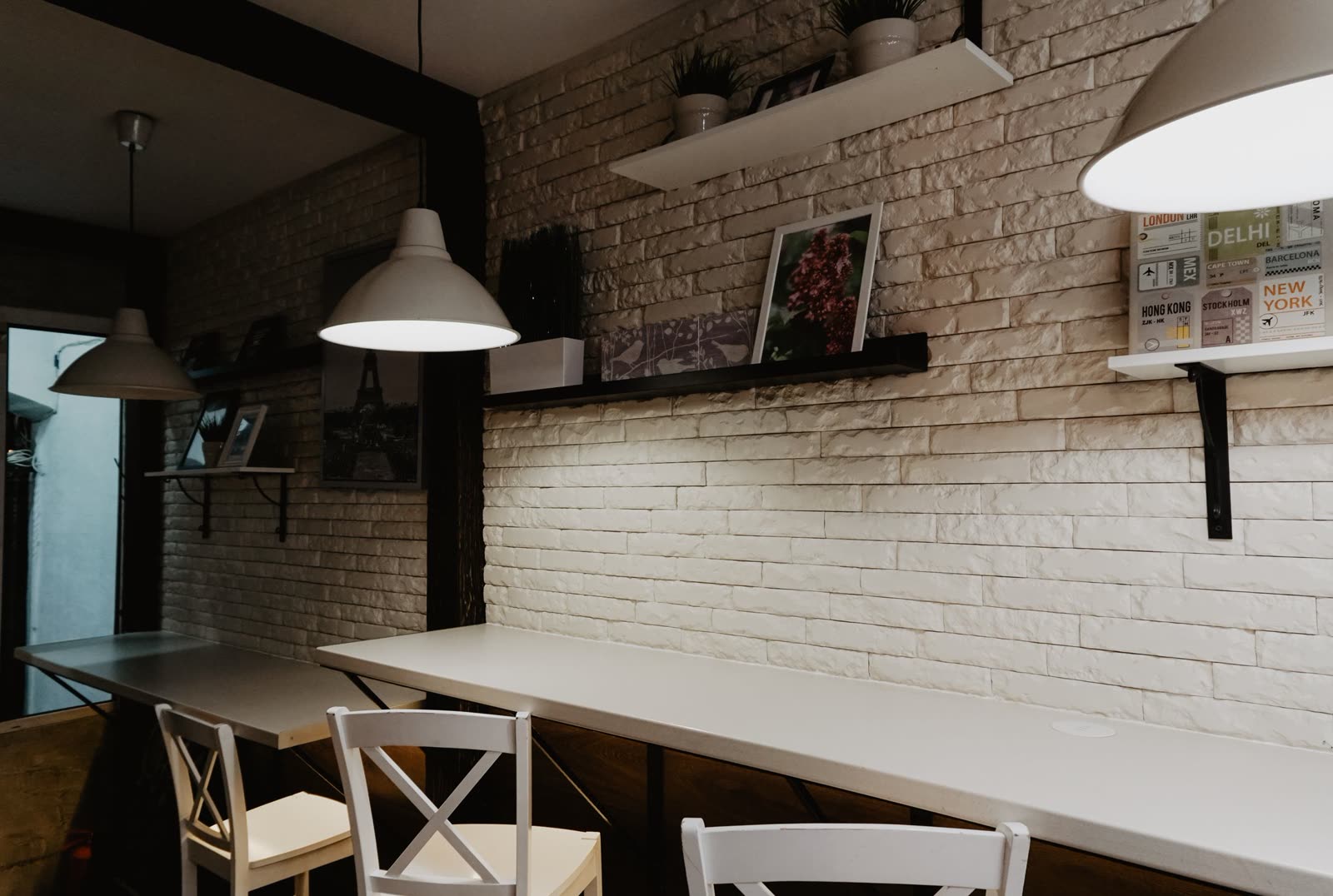 A brick wall of framed pictures above a banquette, lit by table lamps and a candle