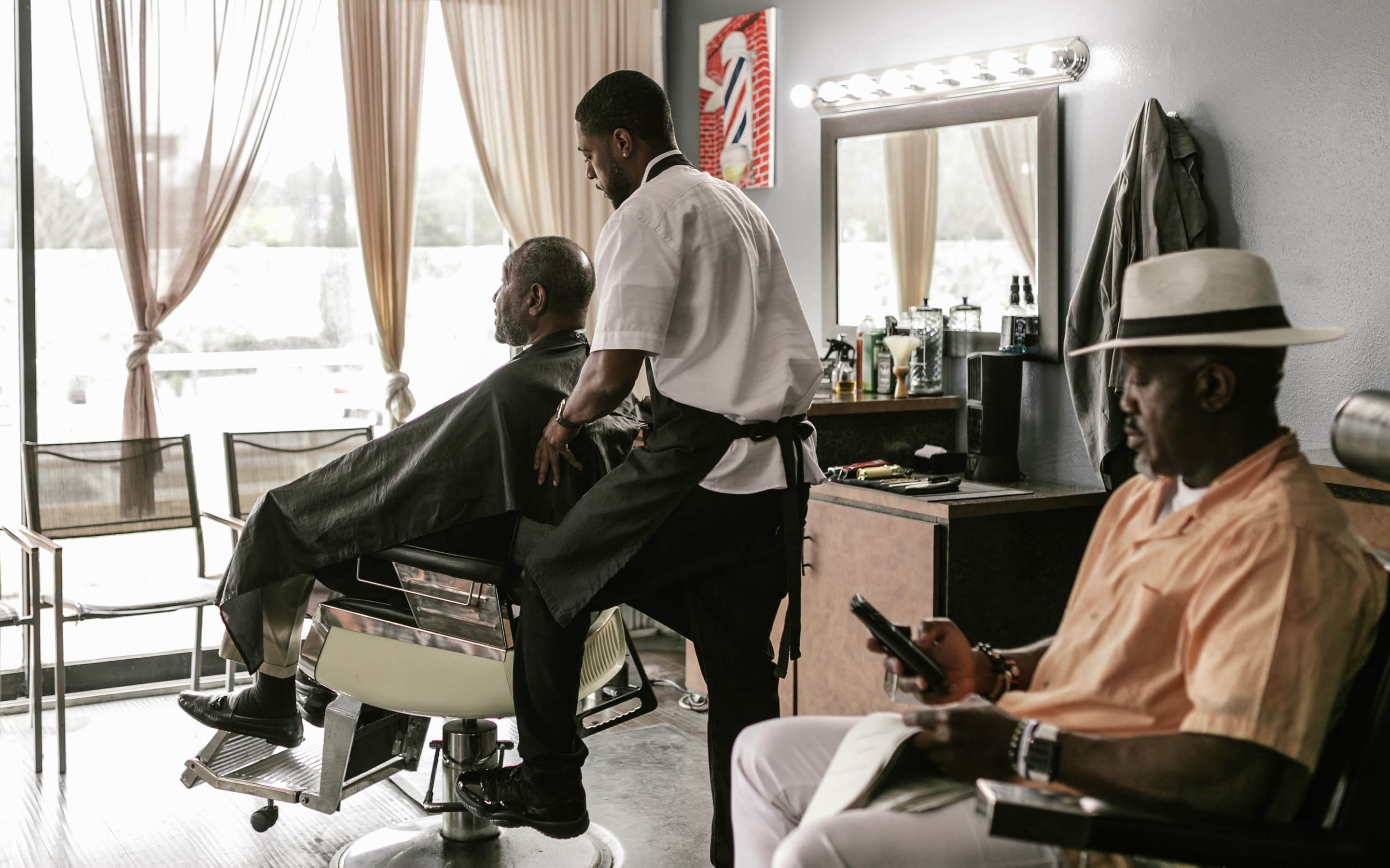 Barber working at a chair by the front window while the next client waits