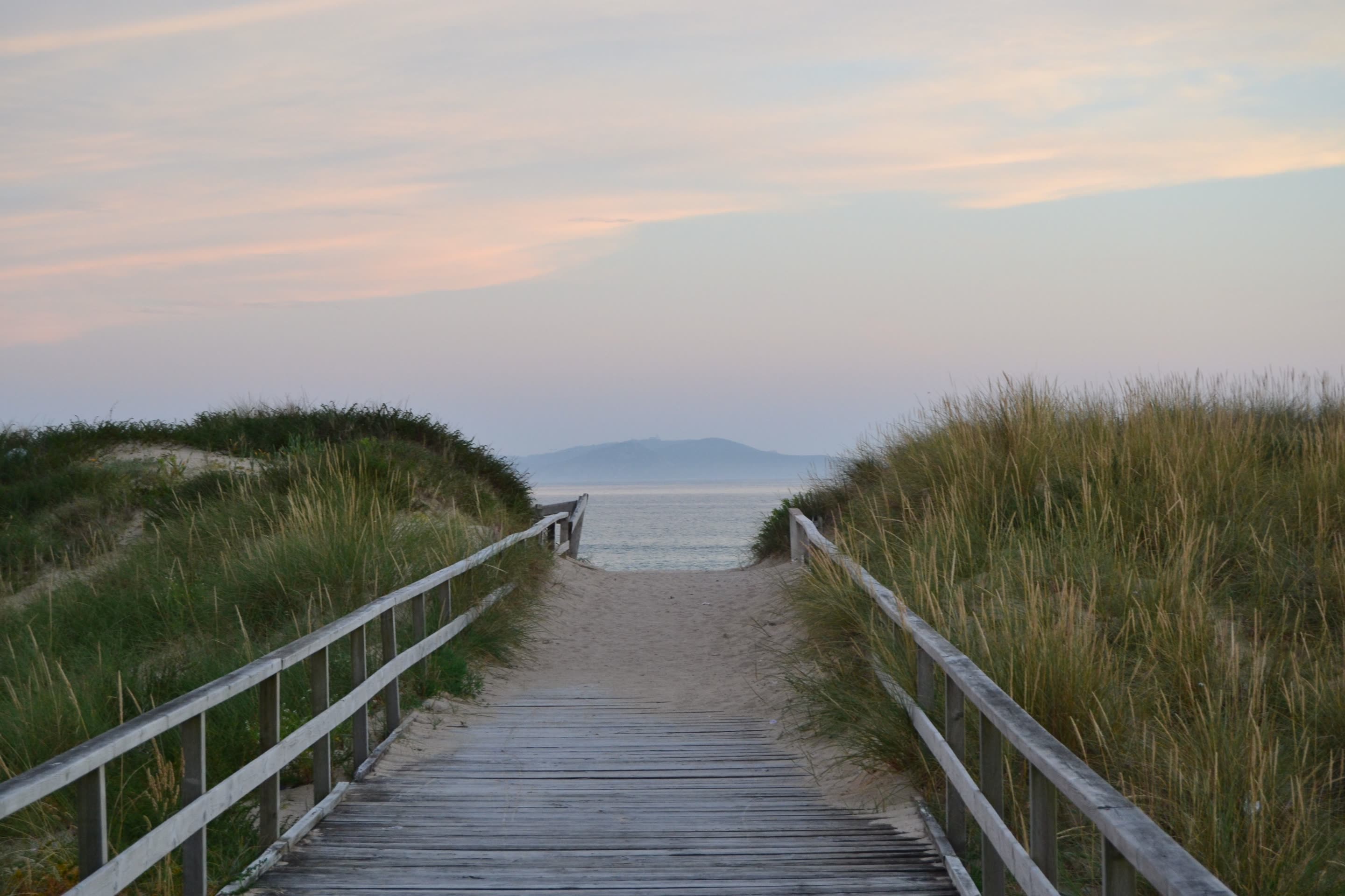 Wooden boardwalk between dune grass leading to the ocean at dusk