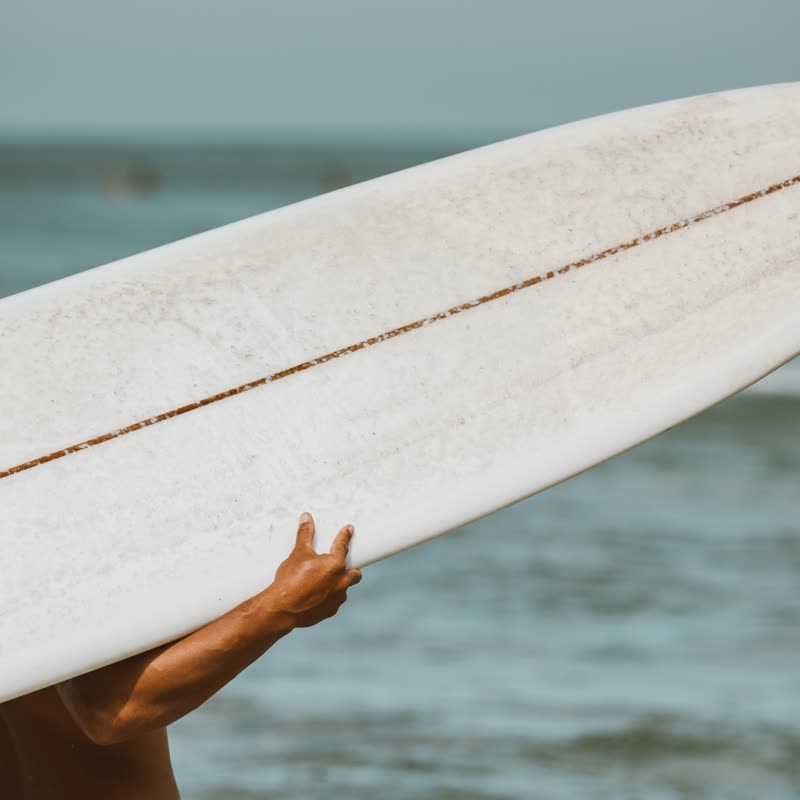 A white longboard held overhead against the sea