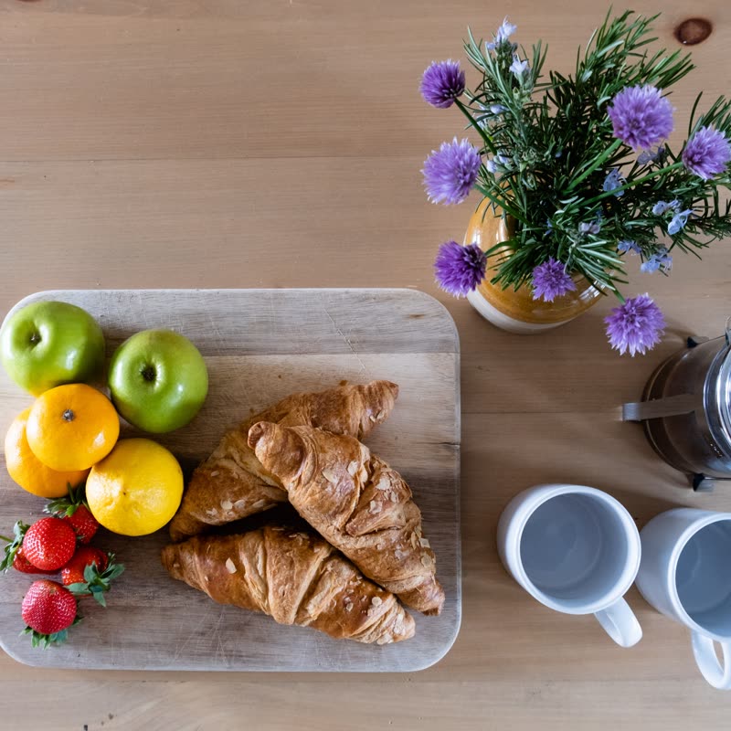 Croissants, apples, oranges and strawberries on a wooden board