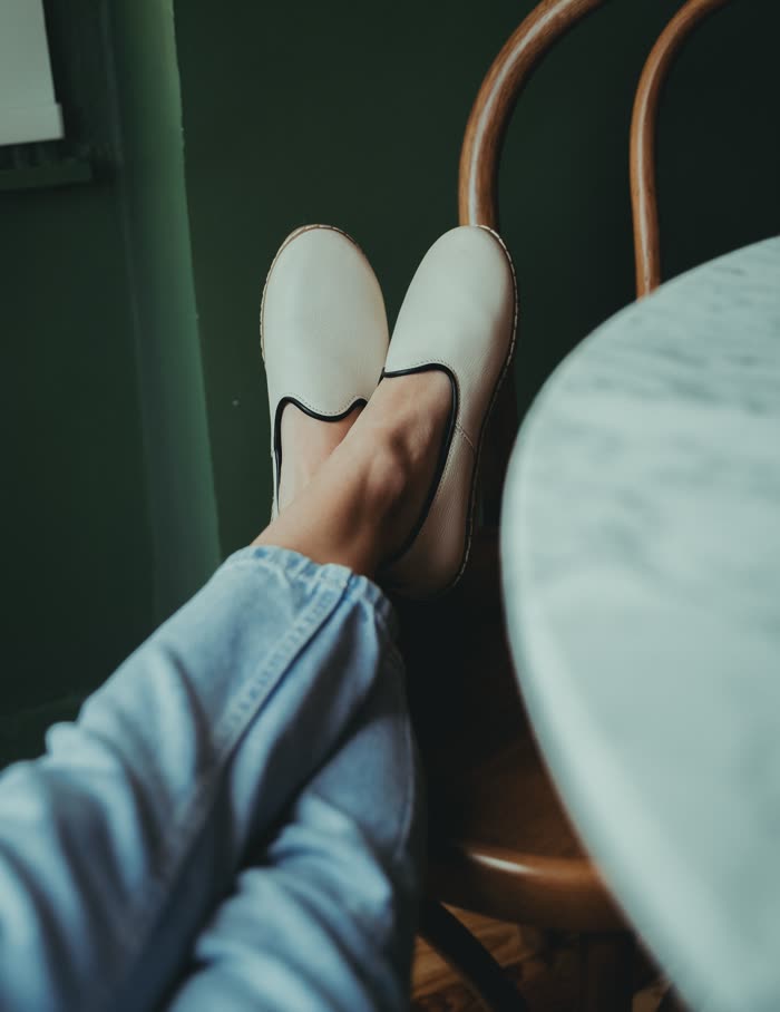 Cream slip-ons crossed at the ankle beside a cafe table