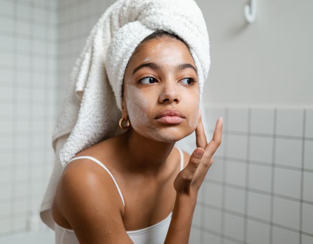 Woman in a towel smoothing cream onto her cheek