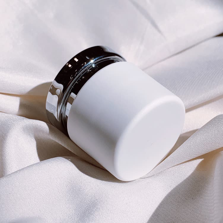 Cedar Leaf Eye Balm in a white jar resting on linen