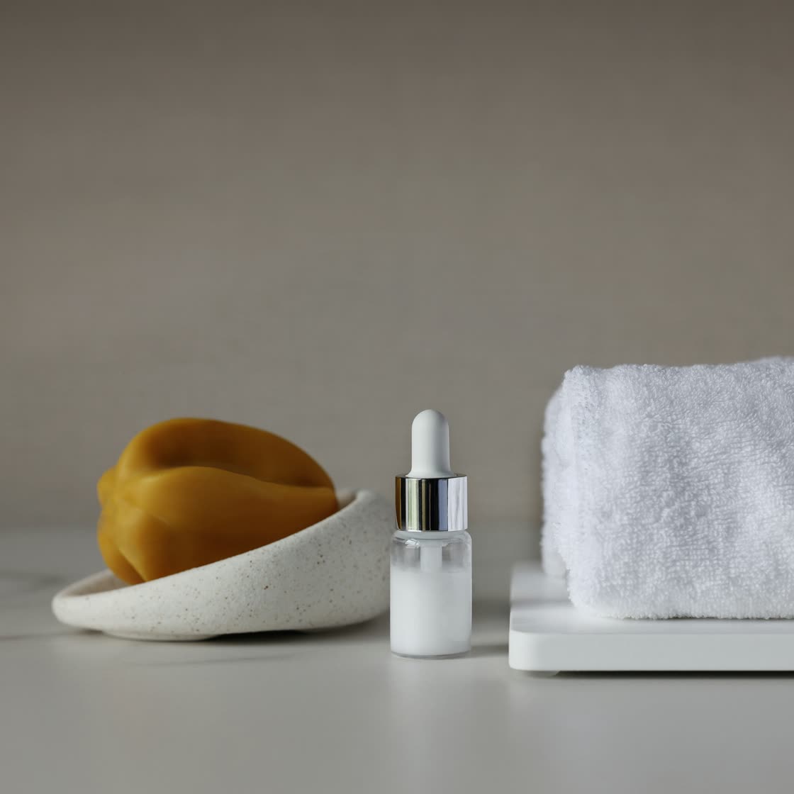 A small white dropper vial beside a sea sponge and a folded towel