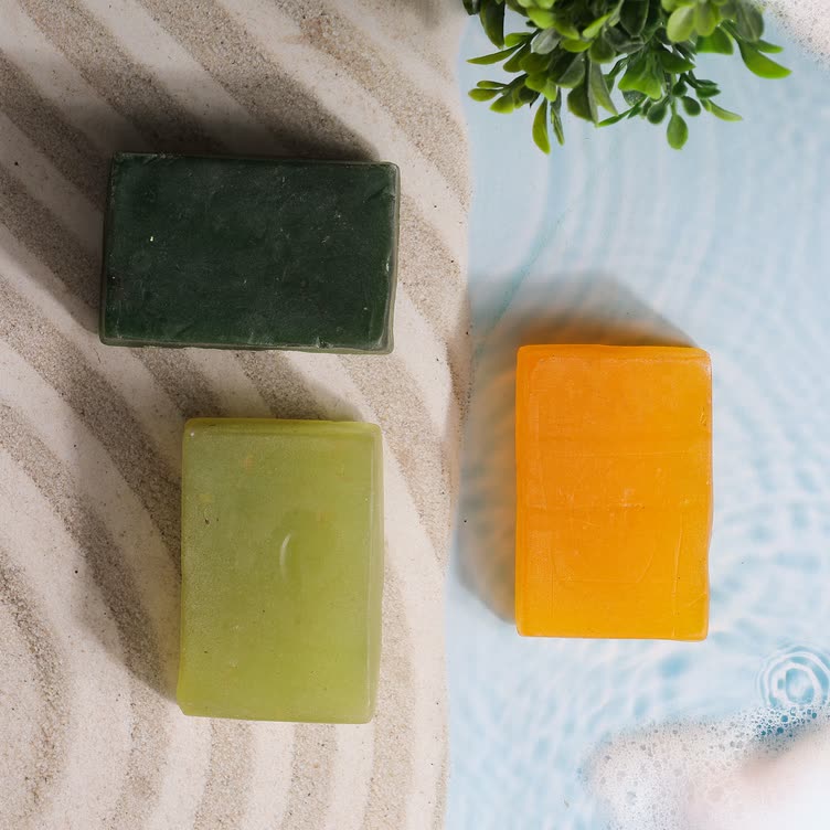 Three soap bars in dark green, sage and orange on sand