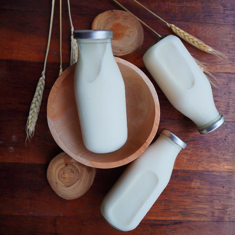 Three glass bottles of body milk in a wooden bowl
