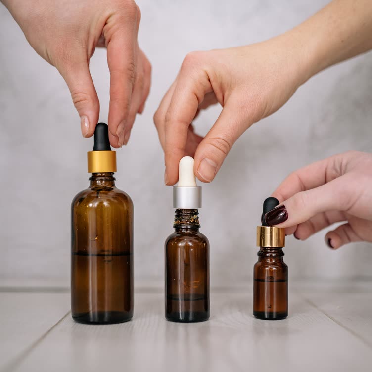 Hands lifting droppers from three amber glass bottles