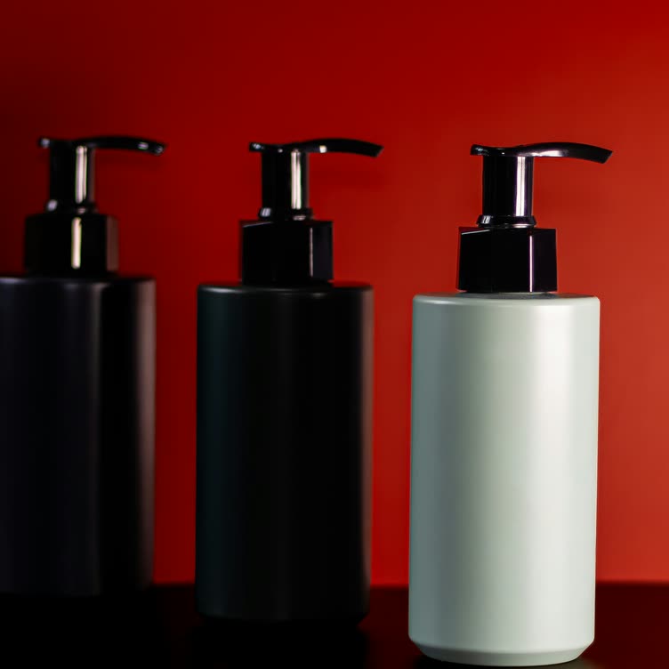 Three unlabeled pump bottles, two dark and one pale grey, against a red wall