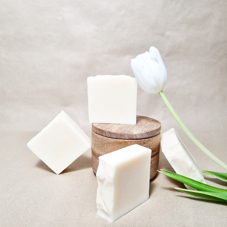 White unscented soap bars stacked by a wooden dish