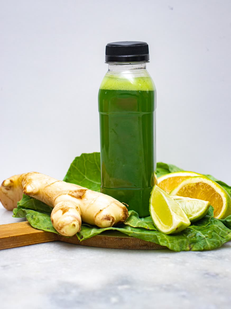 A bottle of green juice beside ginger, lime and orange on a leaf