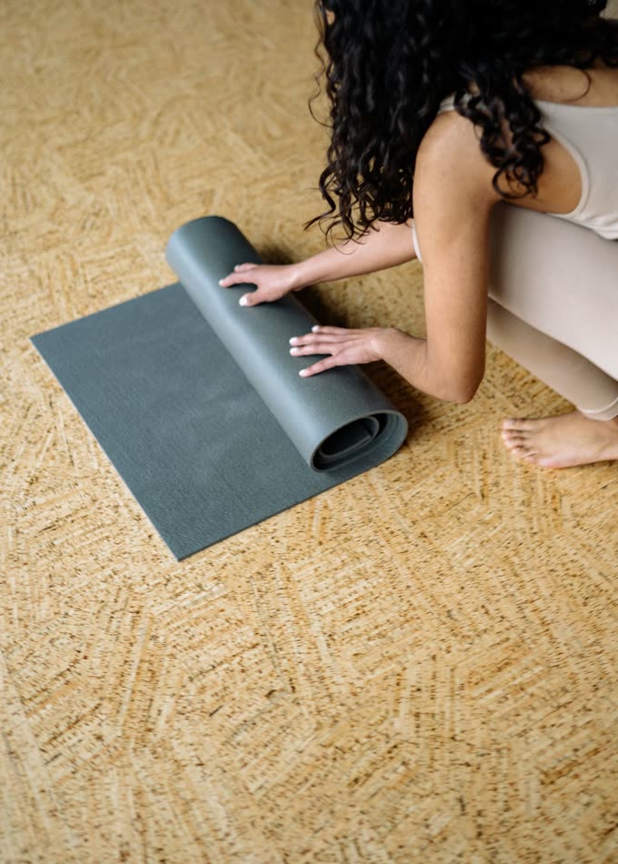 Rolling up a thin grey mat on a woven floor