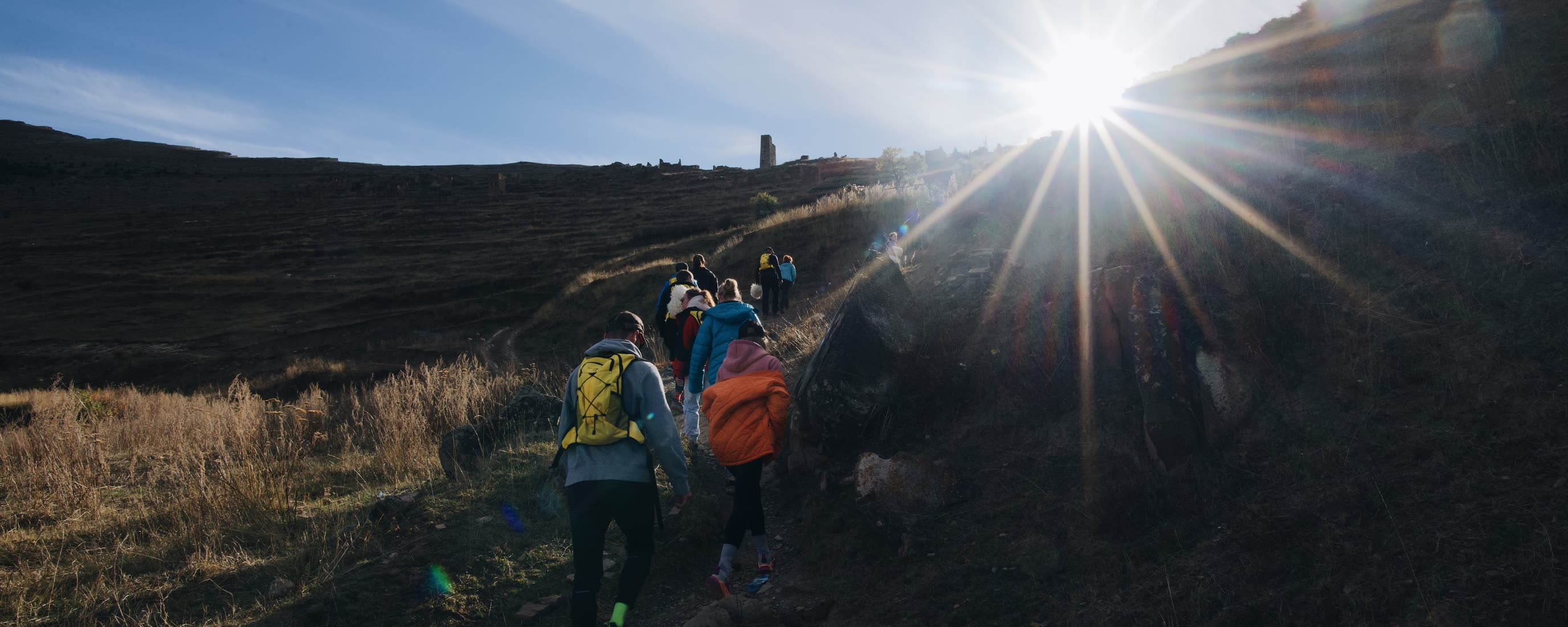 Hikers climbing a dark foothill ridge toward the rising sun