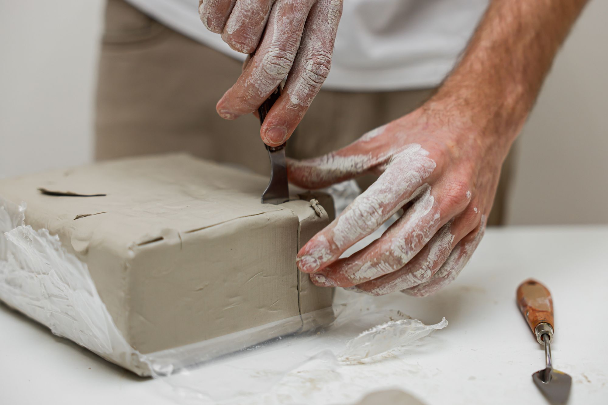 Hands cutting a block of modeling clay