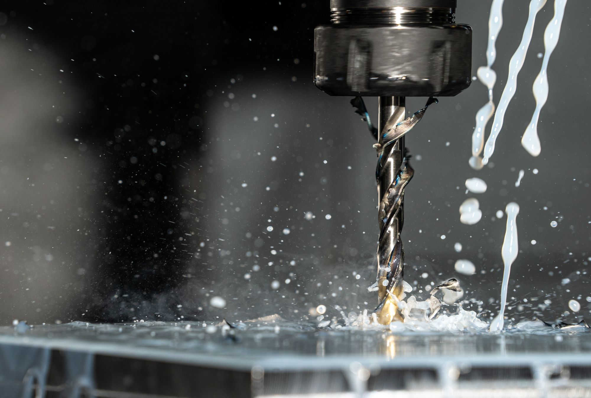 A drill bit cutting metal with coolant splashing