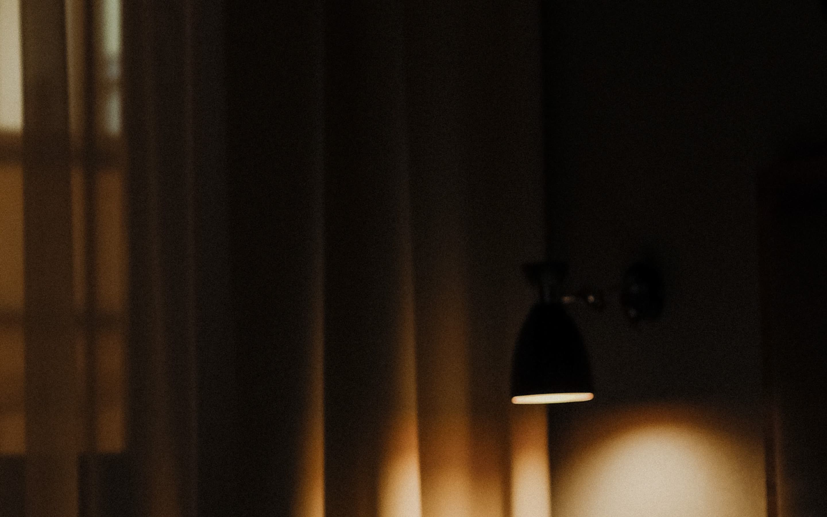 A wall lamp lighting sheer curtains in a guest room at night