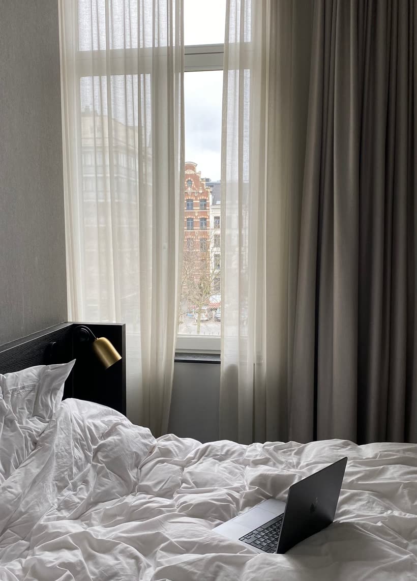 Unmade bed beside a tall curtained window