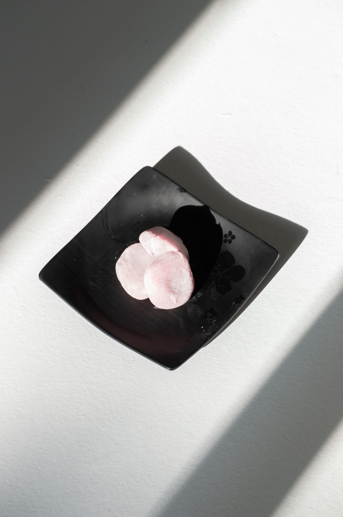 黒い皿にのせた桃色の生菓子