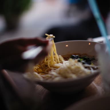 暗い丼から麺を持ち上げる箸