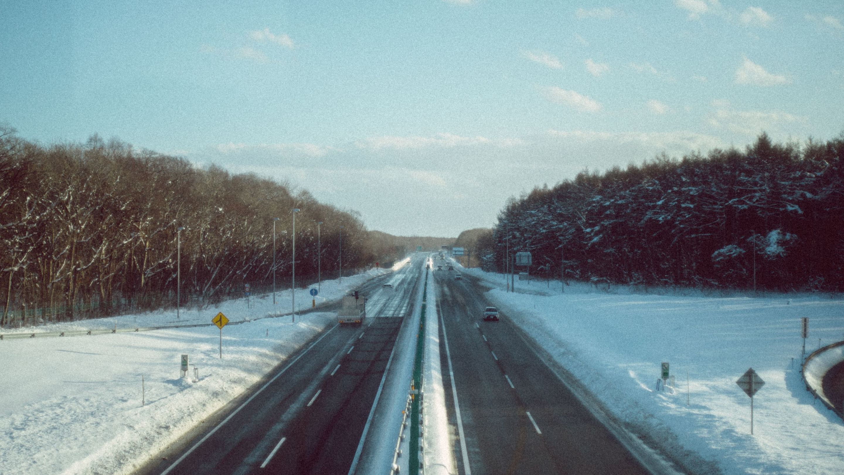 雪におおわれた林のあいだを走る冬の高速道路