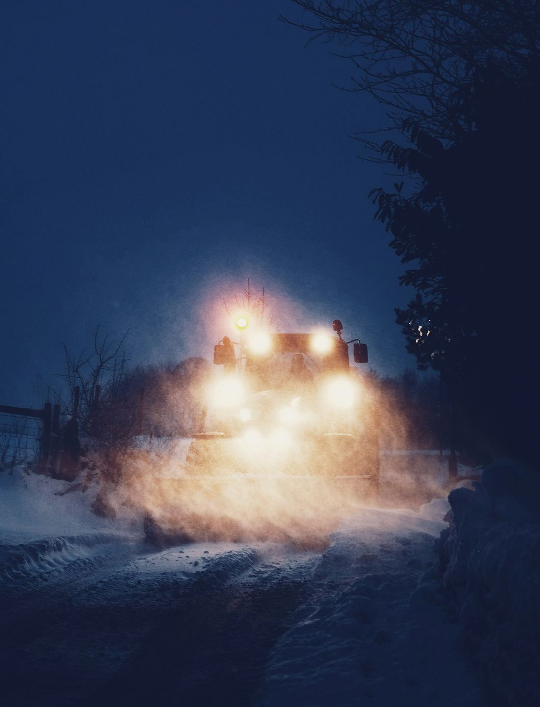 夜の雪道でライトをつけて雪を飛ばす除雪車