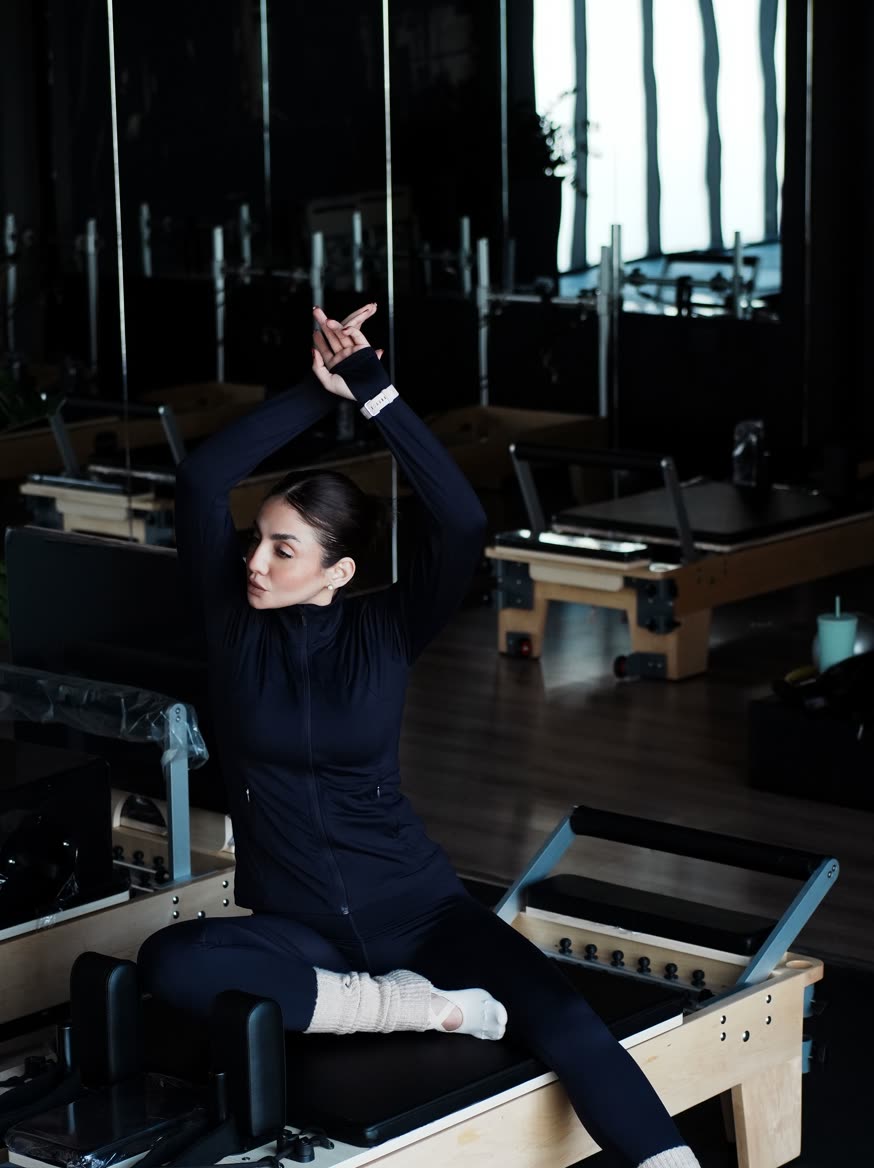 照明を落とした部屋で、リフォーマーに座って腕を上げる人