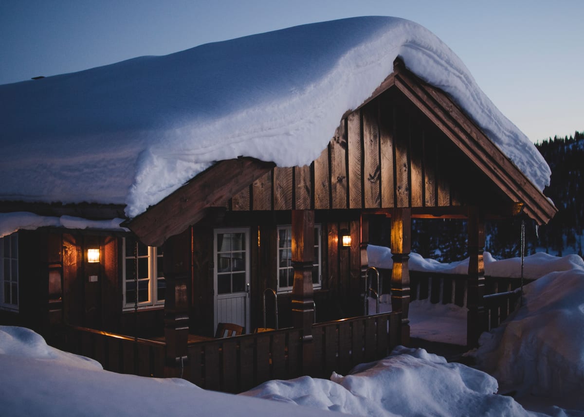 屋根に雪を積んだ木の小屋に明かりがともる