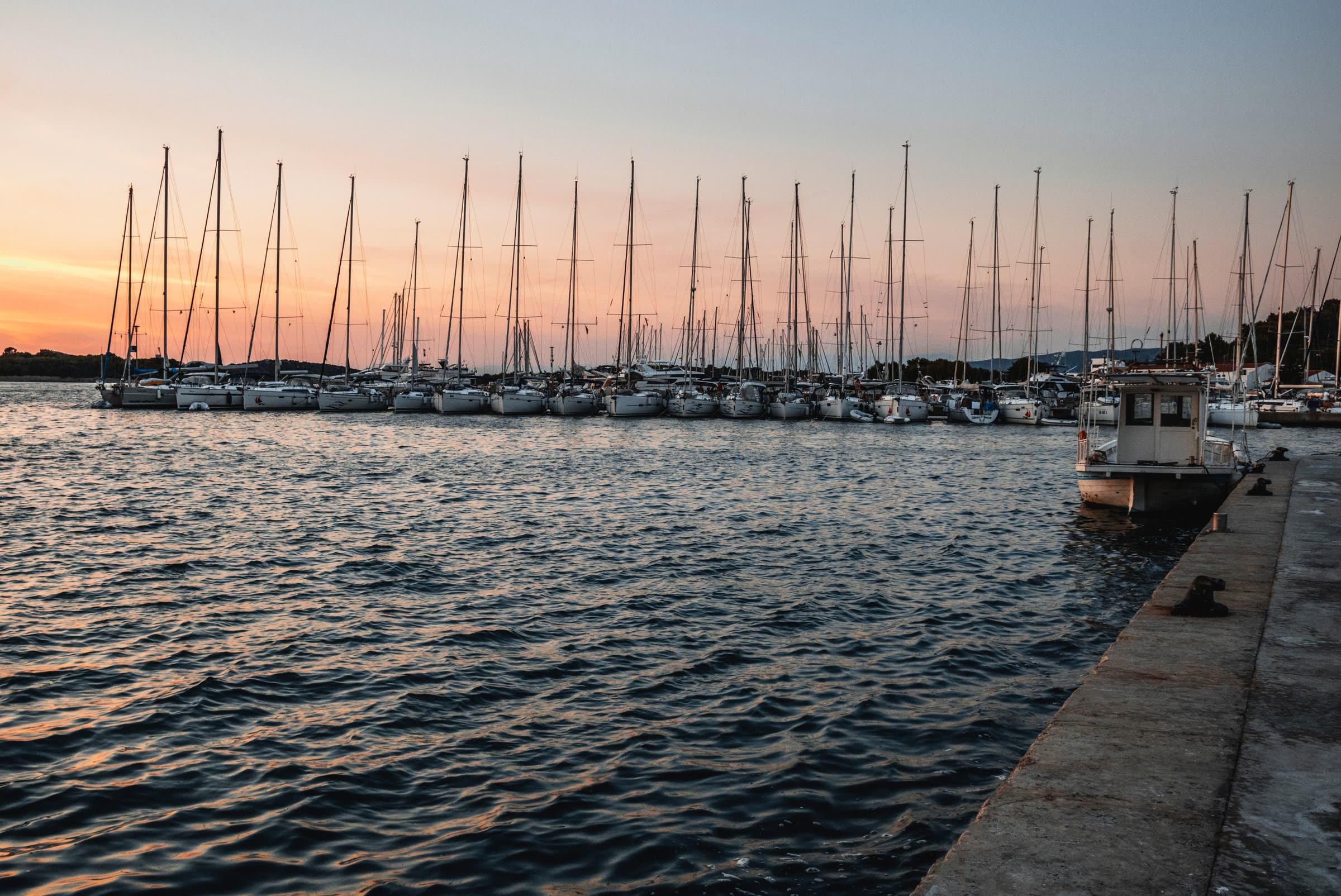 Sailboats moored along a harbor wall at dusk