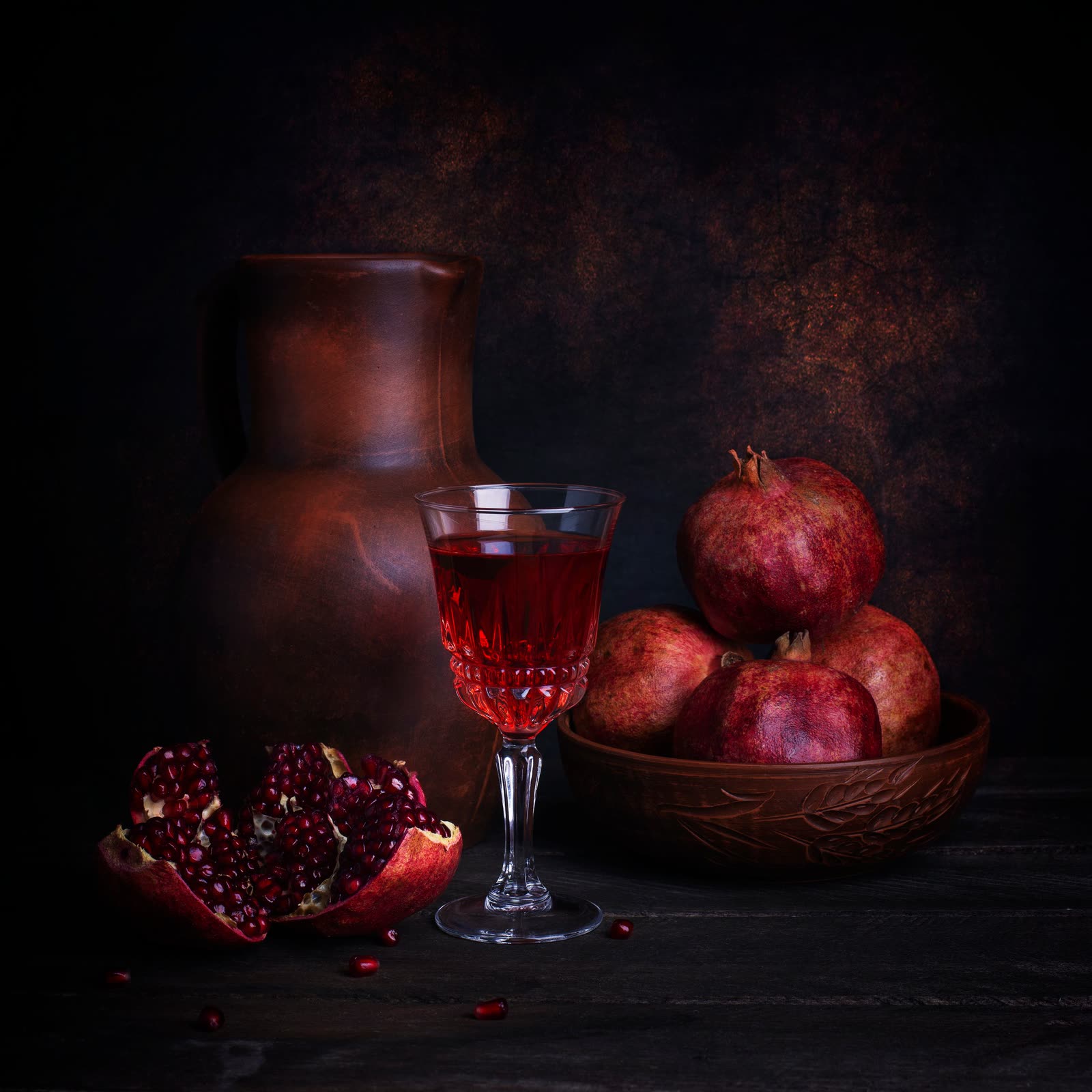 A glass of red wine beside pomegranates on a dark table