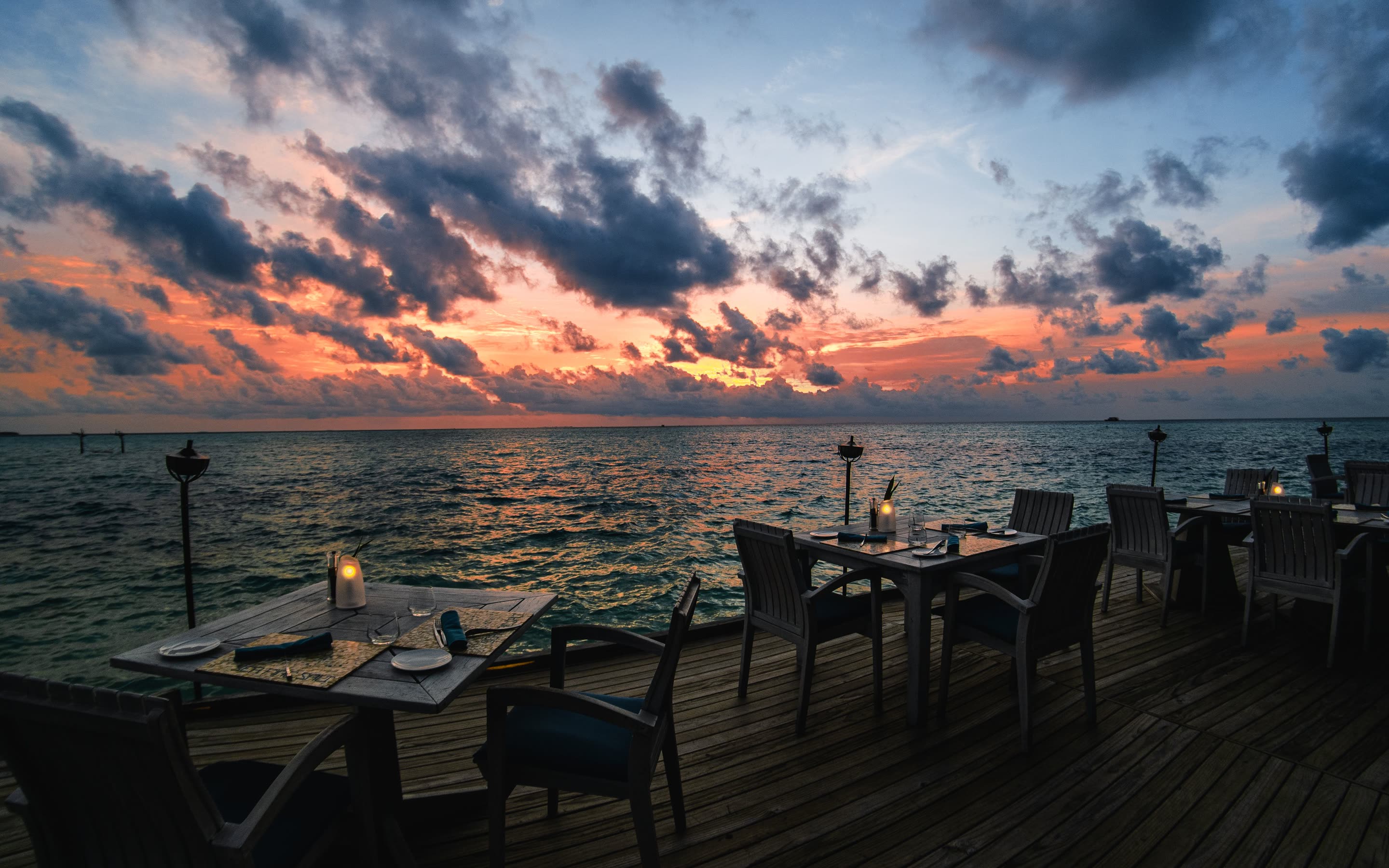 Dining tables on a waterfront deck at sunset