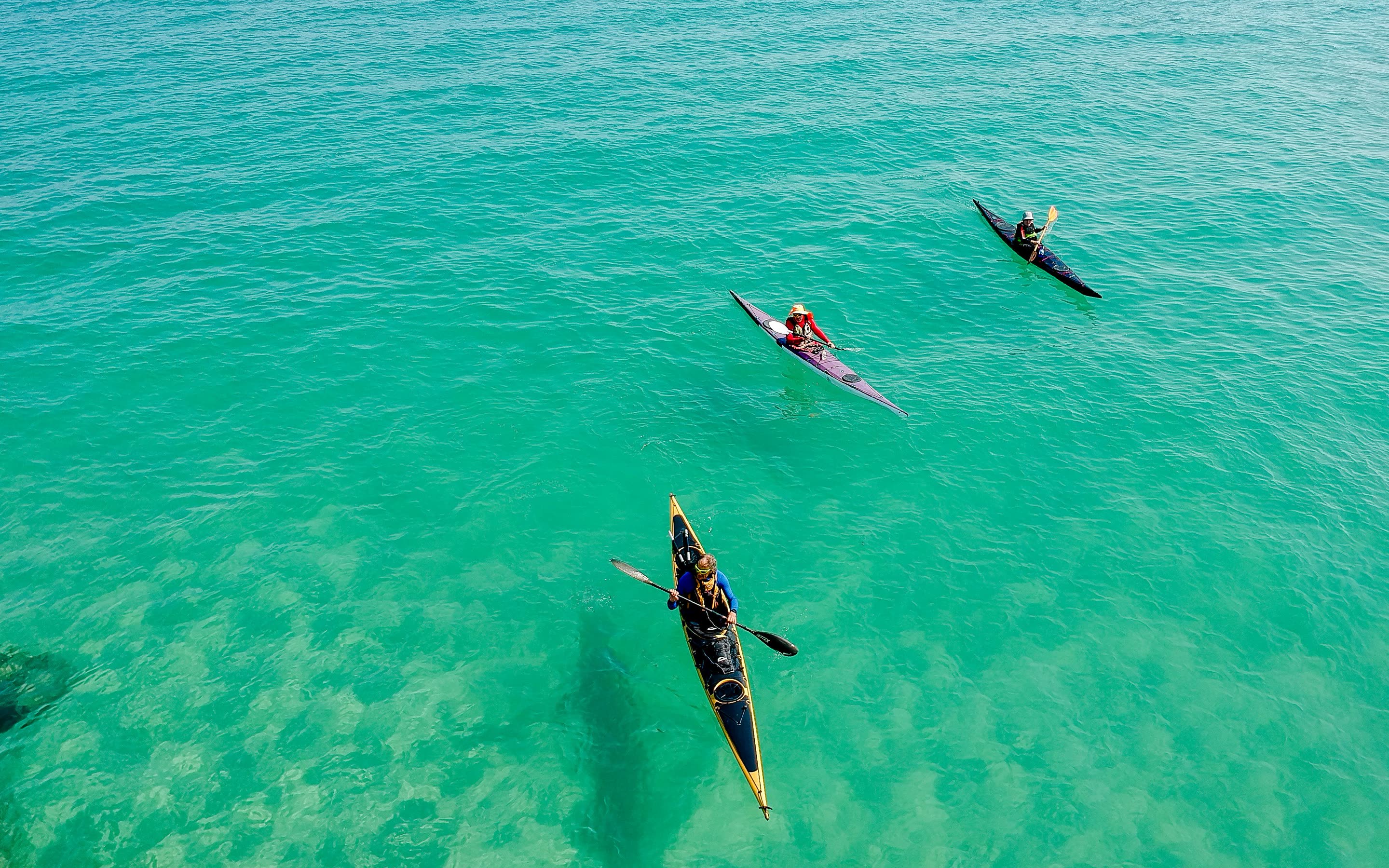 Three sea kayaks crossing clear green shallows, seen from above