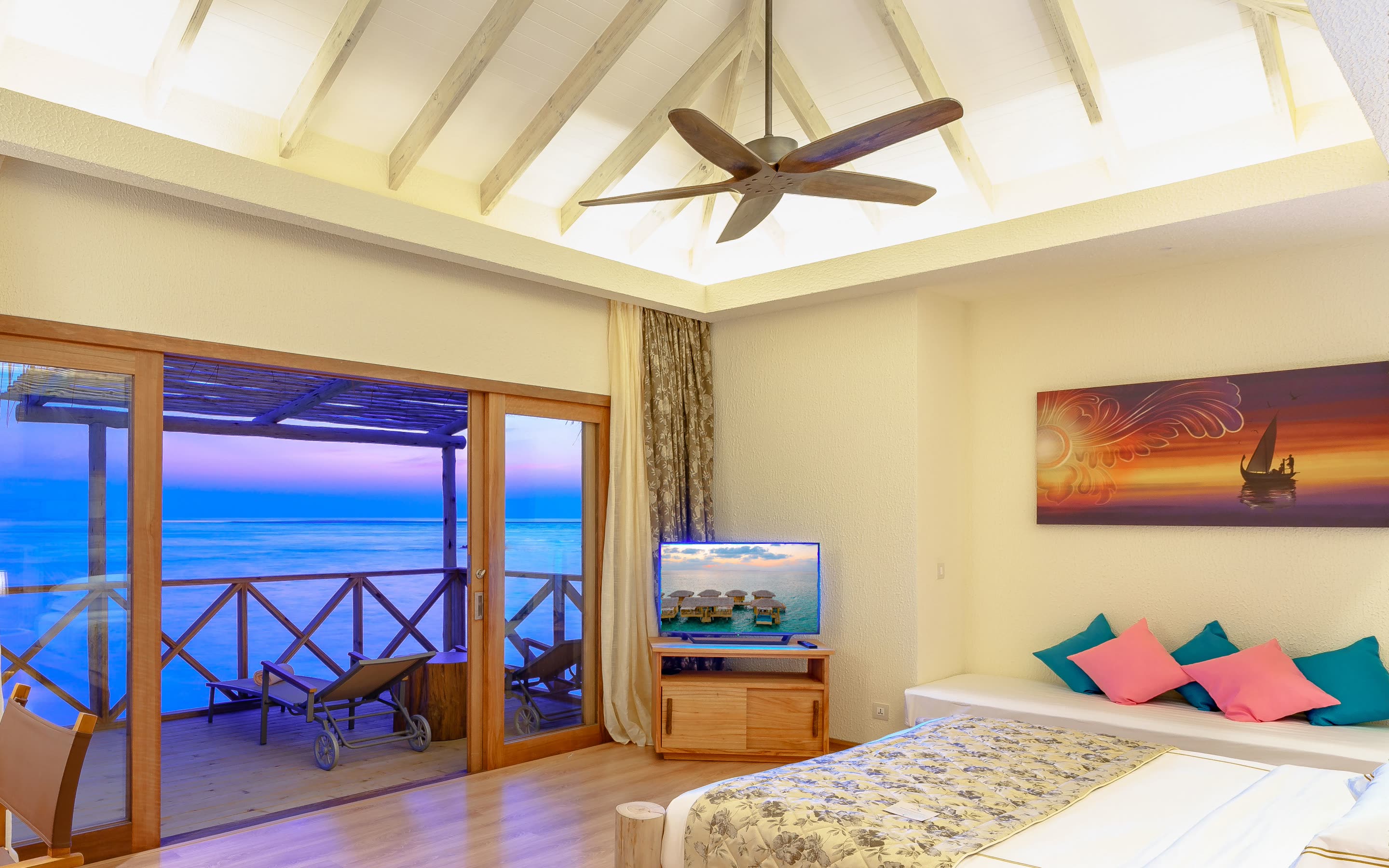 Villa bedroom with a ceiling fan and glass doors open to the deck at dusk