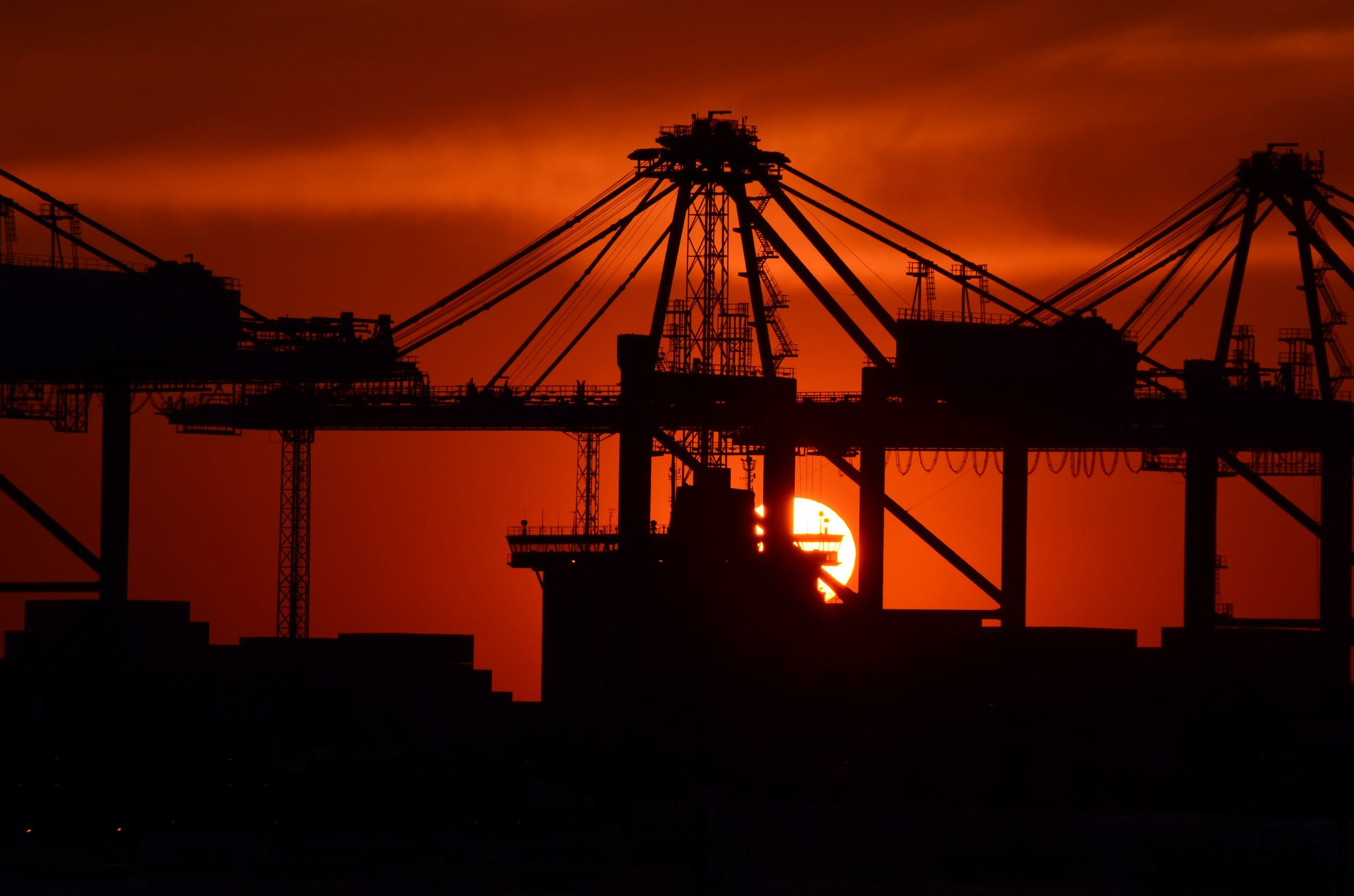 A container crane in silhouette against an orange sky