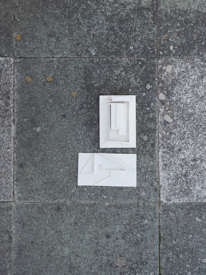 Two small white massing models laid on concrete
